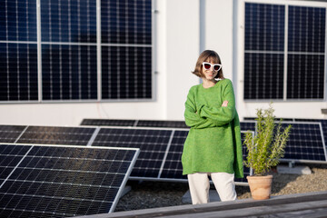 Portrait of a happy woman stands with green plant on a rooftop with a solar power plant installed...
