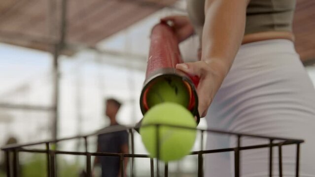 Big yellow tennis balls fall into full basket close up. Person prepare game slow motion. Man tidy after sport play. Many hands pick a lot of inventory equipment. Clean padel court closeup. Tube pour.