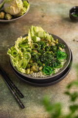 Green bowl with beautifully designed healthy food - rice, vegetables, herbs and seaweed in Asian style. Food styling with products in green. 
