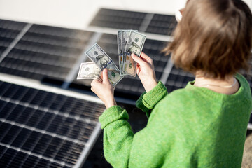 Woman counts dollar banknotes saved due to the generation of energy from a solar power plant...
