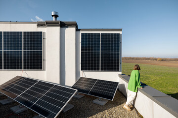 Woman on the rooftop of her house with a solar power plant installed on it. Happy owner of...
