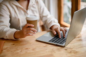 Chilling young Asian woman sipping coffee and using her laptop in a coffee shop.