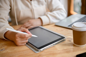 Fototapeta premium Close-up image of a woman holding stylus pen and using her digital tablet at a table