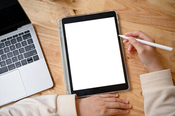 Top view of a woman holding stylus pen and using her digital tablet at a table.