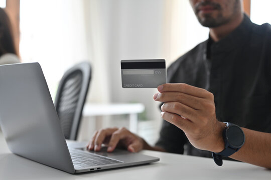 Close up and cropped image of Young businessman with beard holding credit card and use a laptop.