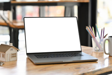 Blank screen of Laptop computer and mock up house at the wooden office desk.