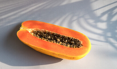 Ripe papaya fruit cut into half on light background with palm leaves shadow. Copy space.