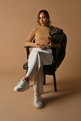 Full-length portrait of Young Asian woman sitting on modern armchair along with draping the coat on...