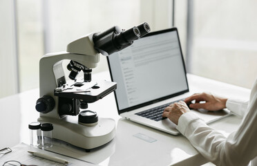 Scientist or student using laptop computer and microscope