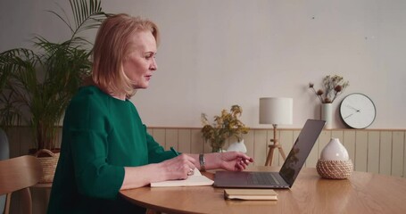 Beautiful middle-aged welness coach consulting clients online, using laptop webcam. Stylish beauty salon setting.