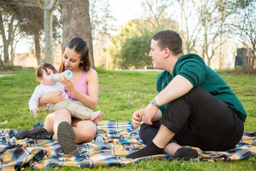 young couple sitting on the lawn while the woman feeds her baby a baby's bottle