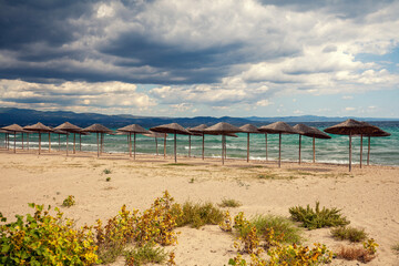 Seascape with dramatic cloudy sky and sun umbrellas. Straw umbrellas on a deserted beach in inclement weather