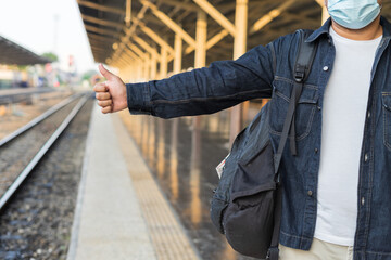 Fototapeta premium Young asian man traveler backpack in the train station. Backpacker male wear hat and denim jacket at the railway. Travel concept. The concept of a man traveling alone.