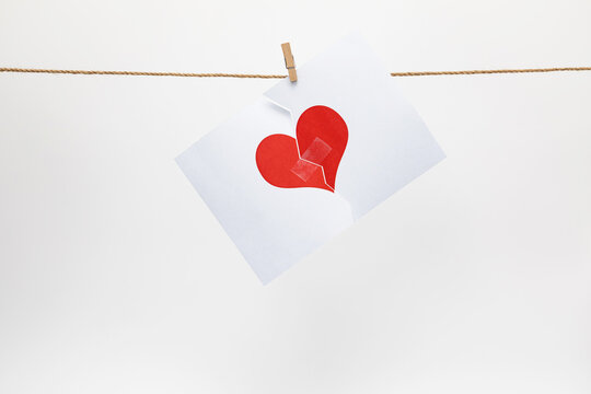 Broken love heart hanging on a rope on a white background