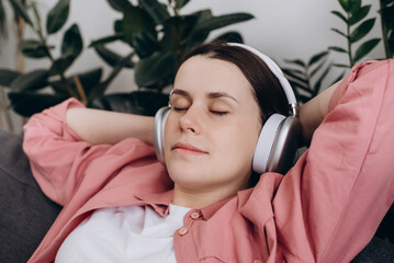 Close up of mindful happy young caucasian female 20s wearing wireless headphones, listening...