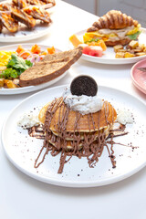 Chocolate drizzling on cut pan cake with other breakfast dishes in the background. 