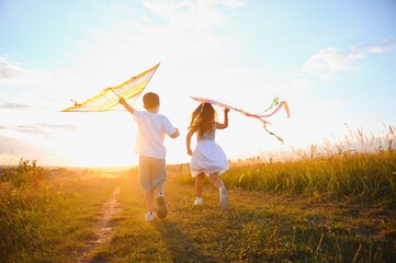 Happy children launch a kite in the field at sunset. Little boy and girl on summer vacation.