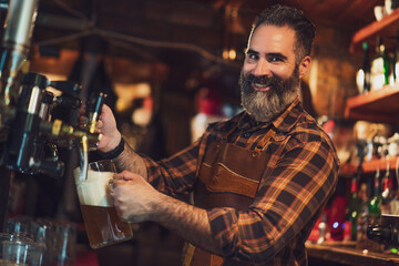 Portrait of cheerful barmen at pub. He pours beer into a beer glass.