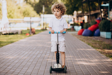 Cute little boy with curly hair riding scooter