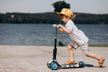 Cute little boy with curly hair riding scooter © Petro