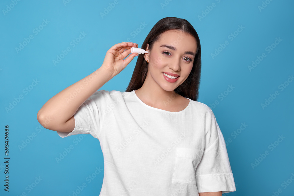 Canvas Prints Young woman using ear drops on light blue background