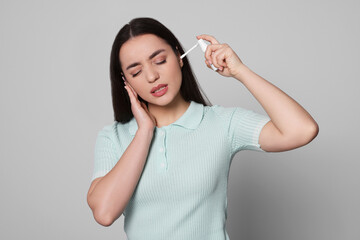 Young woman using ear spray on light grey background