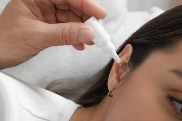 Senior man dripping medication into woman's ear on sofa, closeup
