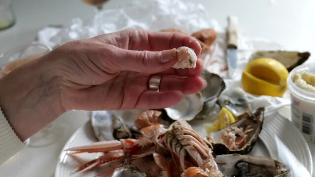 Woman cleaning root canal of prawn above table full of fresh seafood with oyster and lobster from fish market