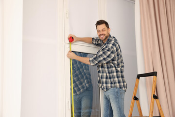 Man measuring window with tape indoors. Roller blinds installation