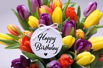 Beautiful bouquet of tulip flowers with Happy Birthday card on light background, closeup