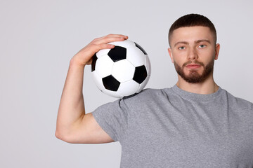 Athletic young man with soccer ball on light grey background