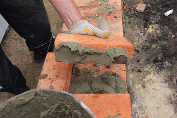 Mason laying house brick wall with mortar on the side of the brick.