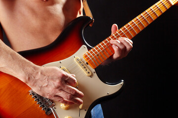 Guitarist playing the sunburst electric guitar on dark stage.