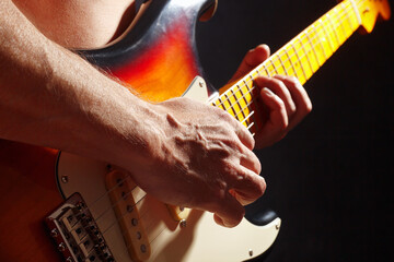 Rock guitarist playing the sunburst guitar on dark stage.