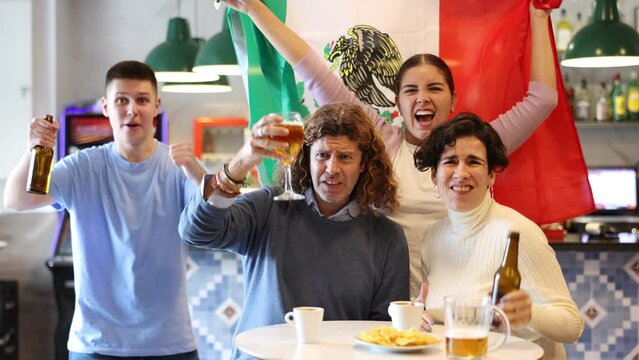 Company of emotional young adult sports fans supporting Mexican team with state flag while resting in pub with beer