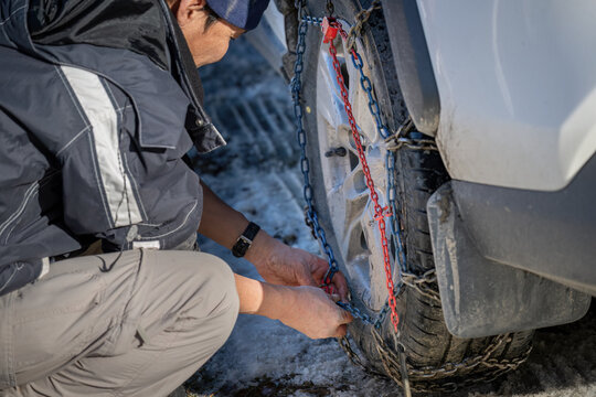 Man putting on snow chains on his car wheels for winter snow condition.