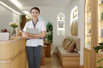 Portrait of young smiling spa salon receptionist holding documents
