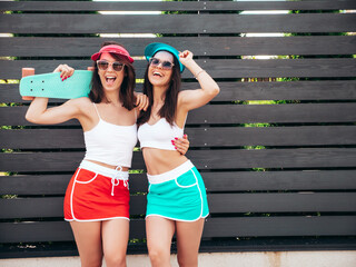 Two young beautiful smiling hipster women posing in the street. Sexy trendy models in summer white...