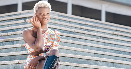 African transgender woman sitting on stairs, listening to audio on her phone