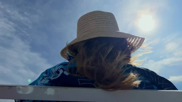 Anonymous blonde woman wearing straw hat on yacht under sun on windy day in summer. Marine adventure. Elderly woman on a voyage. Cruise. Film grain pixel texture. Soft focus. Live camera. Blur.