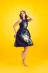 Elegant fashion. Stunning woman in elegant long dress in studio stands on a yellow sunny background.