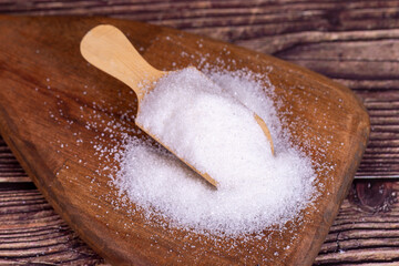 White refined sugar on wood background. Close-up of granulated sugar in wooden spoon