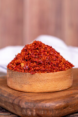 Chilli pepper seedless flakes in wooden bowl. Spices and food ingredients. Close up