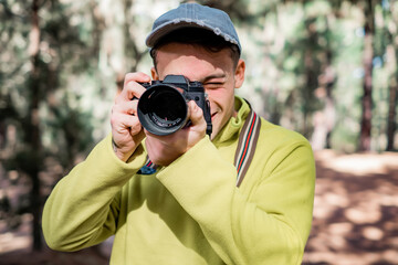 Young photographer with hat working taking capture photo of nature in the woods holding and using his camera in the forest