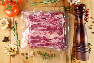 Vacuum packed meat, on a wooden board, steak. Top view. Various spices