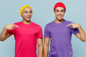 Young smiling couple two friends men wear casual clothes blank print design t-shirts together point index finger on themselves to each other isolated on pastel plain light blue cyan background studio