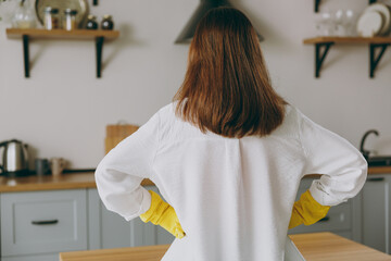 Back rear view young caucasian housewife woman wears casual clothes yellow rubber gloves hold hands...