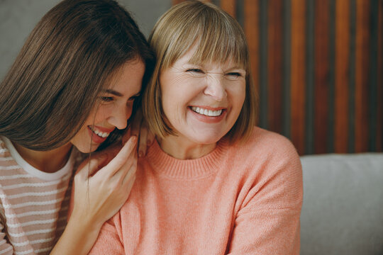 Close up happy fun two adult women mature mom young kid wear casual clothes laughing tell joke hug sit on gray sofa couch stay home flat rest relax spend free spare time in living room Family concept