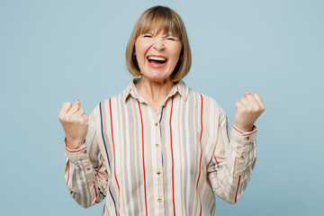 Elderly fun woman 50s years old wear light striped shirt doing winner gesture celebrate clenching...