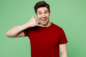 Young cheerful happy caucasian man he wearing red t-shirt casual clothes doing phone gesture like says call me back isolated on plain pastel light green background studio portrait. Lifestyle concept.